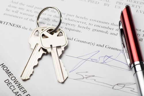 A pair of keys sitting on top of a signed homeowner declaration.