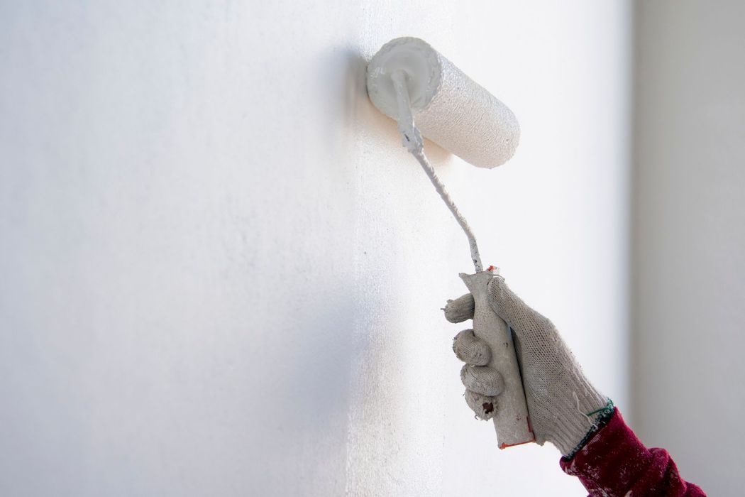 Mano che tiene un rullo per dipingere mentre applica vernice bianca su un muro.