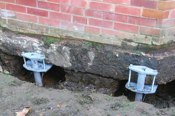 A brick wall with a hole in it and a couple of metal pieces in the ground.