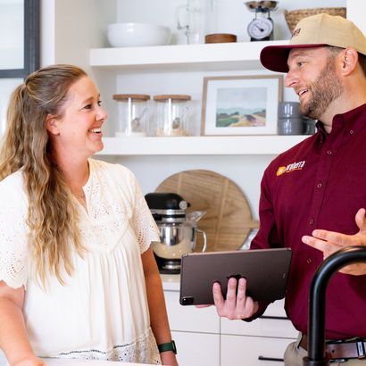 A man is holding a tablet and talking to a woman in a kitchen.