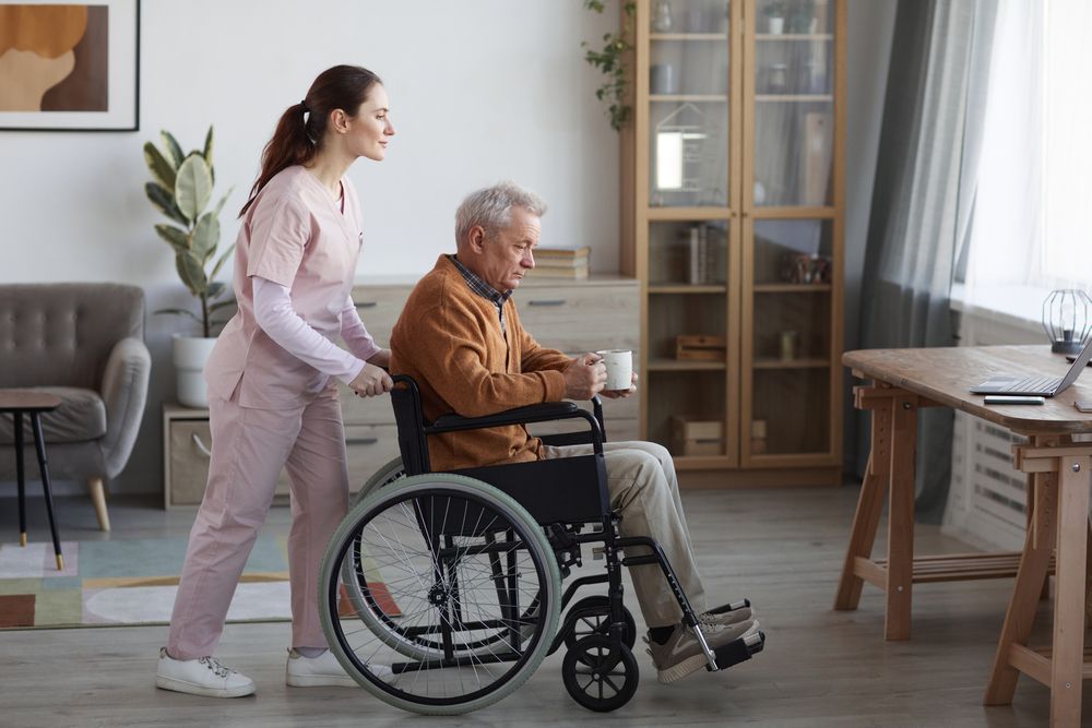 Woman in Pink Scrubs Pushing a Man in a Wheelchair Indoors — Elder Care Connect in Southport, QLD