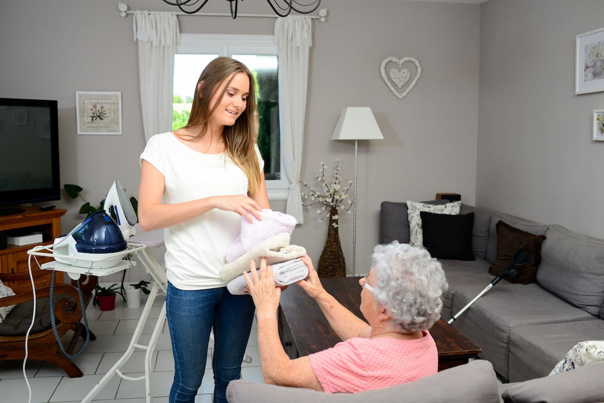 Woman Hands Folded Laundry to An Older Woman in A Living Room — Elder Care Connect in Southport, QLD