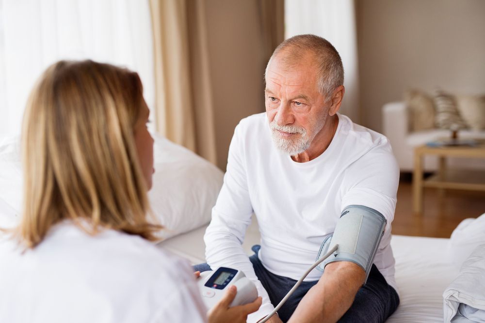 A Healthcare Provider Takes an Older Man's Blood Pressure in a Bedroom — Elder Care Connect in Southport, QLD