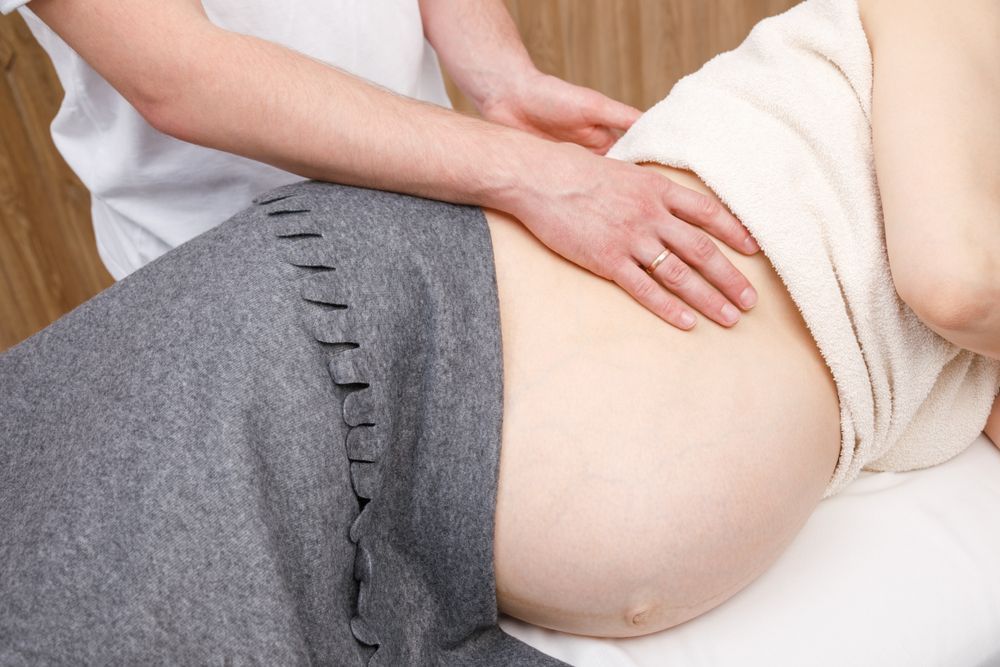 A pregnant woman is getting a massage from a doctor.