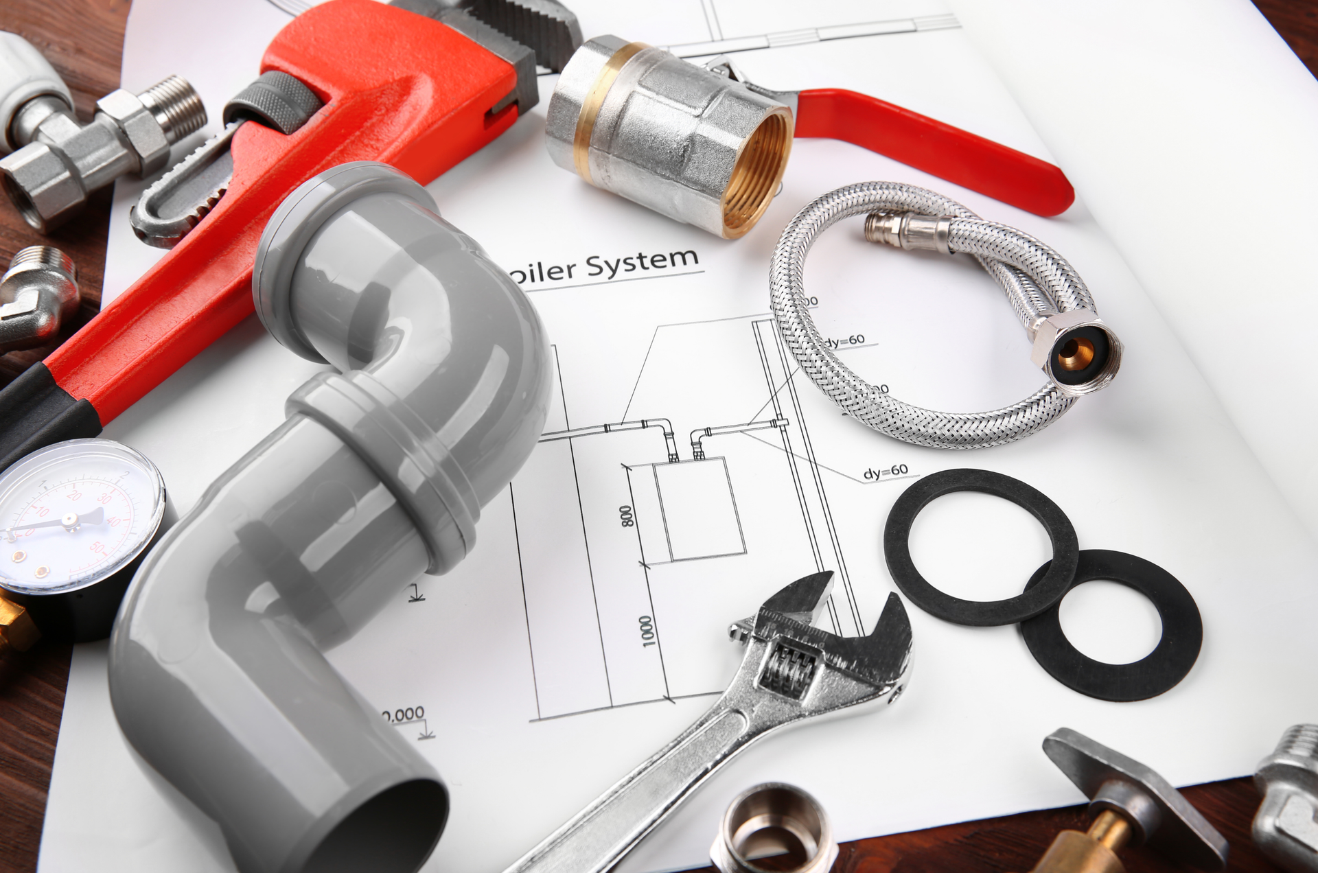 Plumbing tools and parts (wrench, pipe, valve) arranged on a blueprint; red, gray, and silver.
