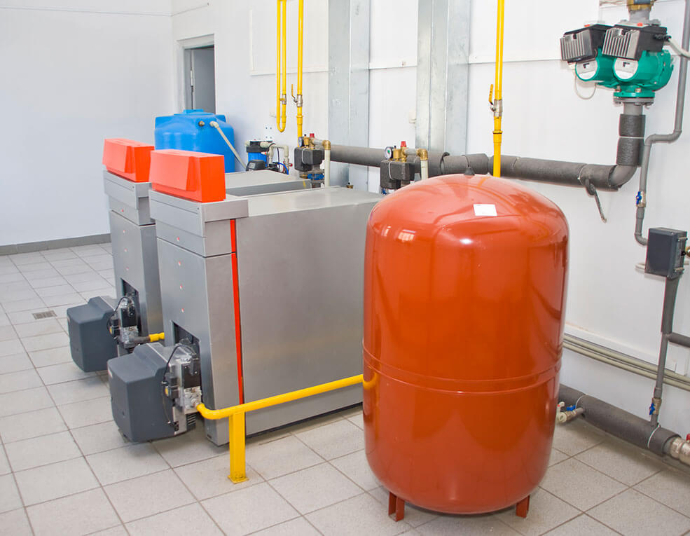 Heating system with two gray boilers, orange tank, and yellow pipes in a utility room.