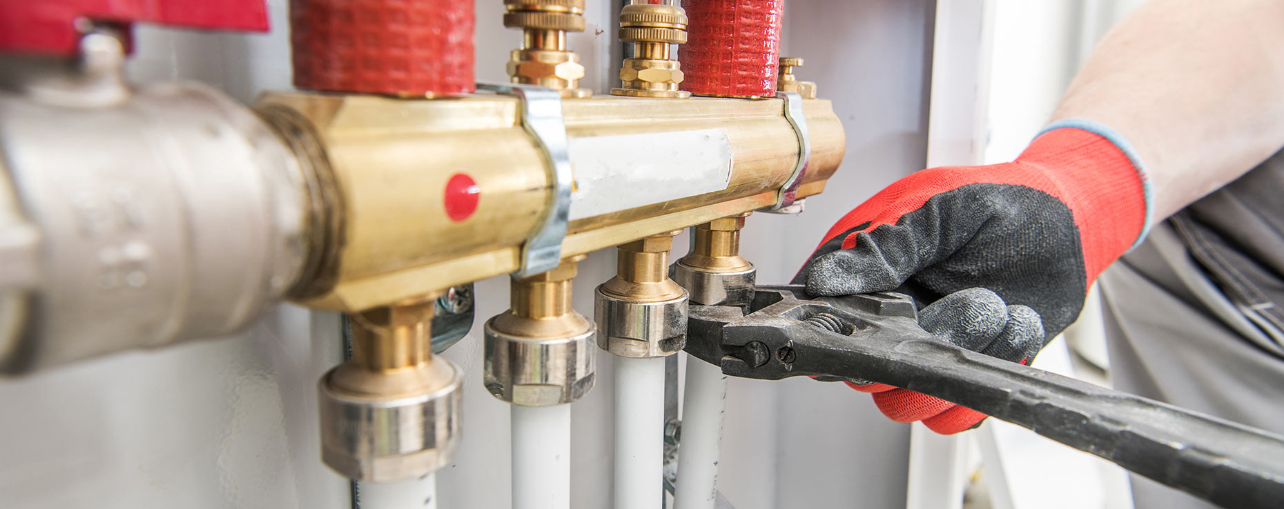 A person wearing gloves using a wrench on a plumbing system.