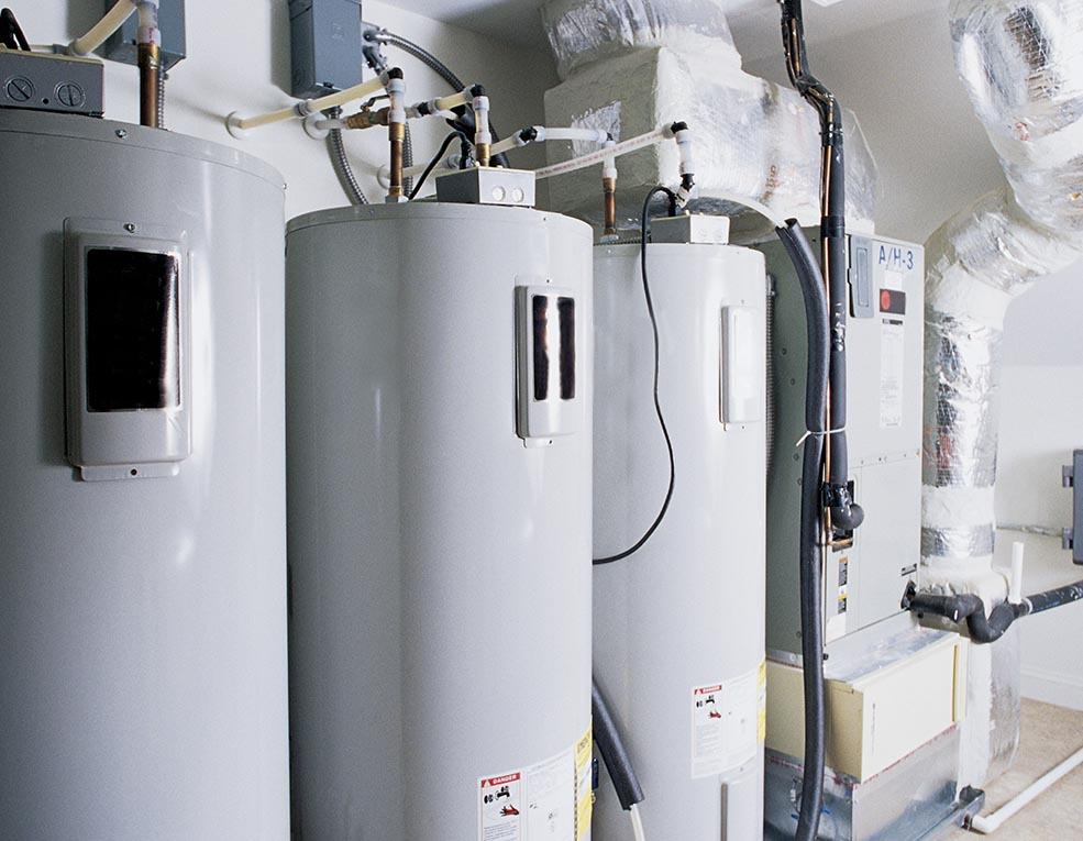 Three gray water heaters and HVAC equipment in an interior utility room.