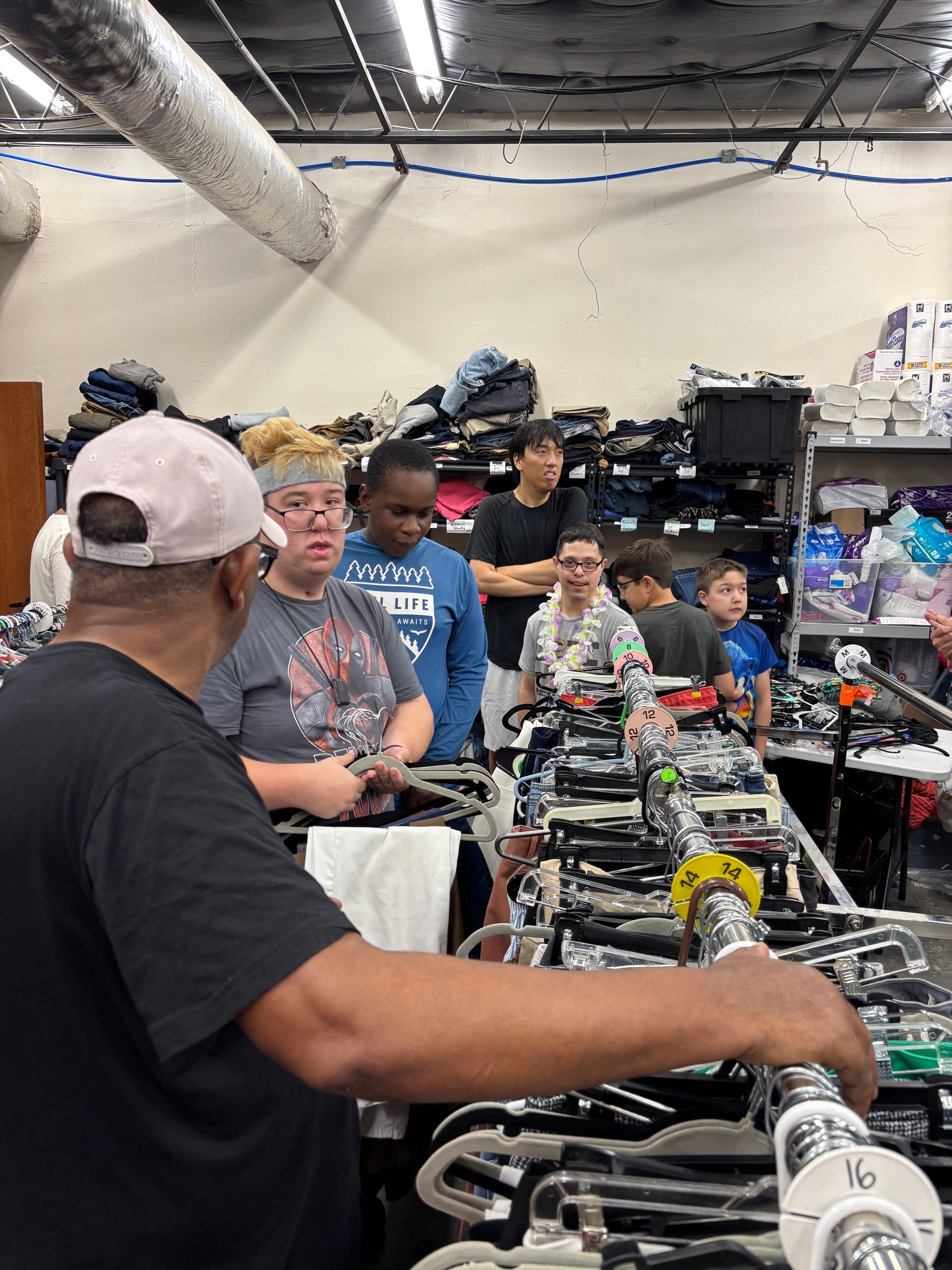 A group of people browsing clothing racks in a store. Man in foreground examines a rack.