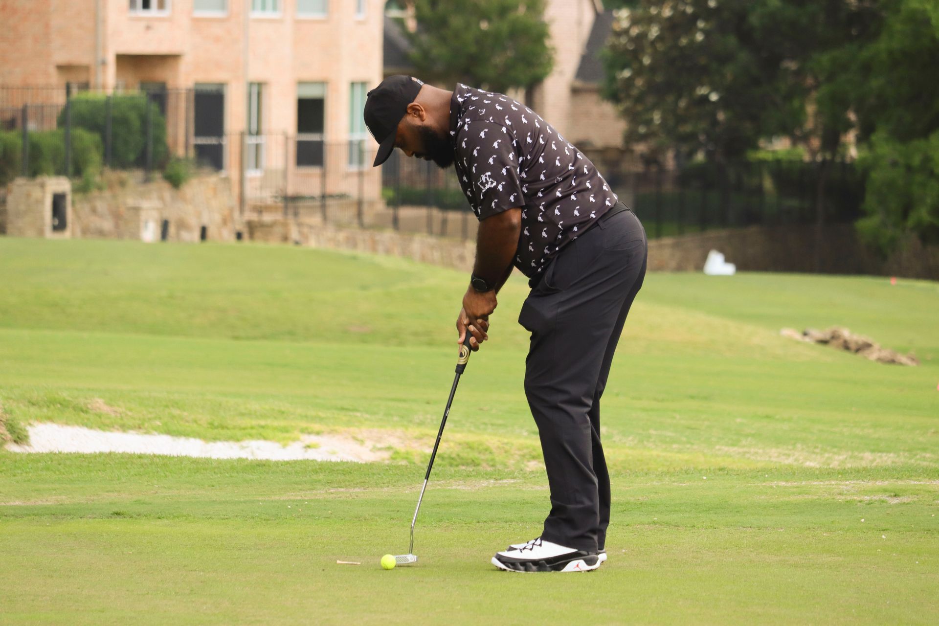 Man in black clothing putting a golf ball on a green course.