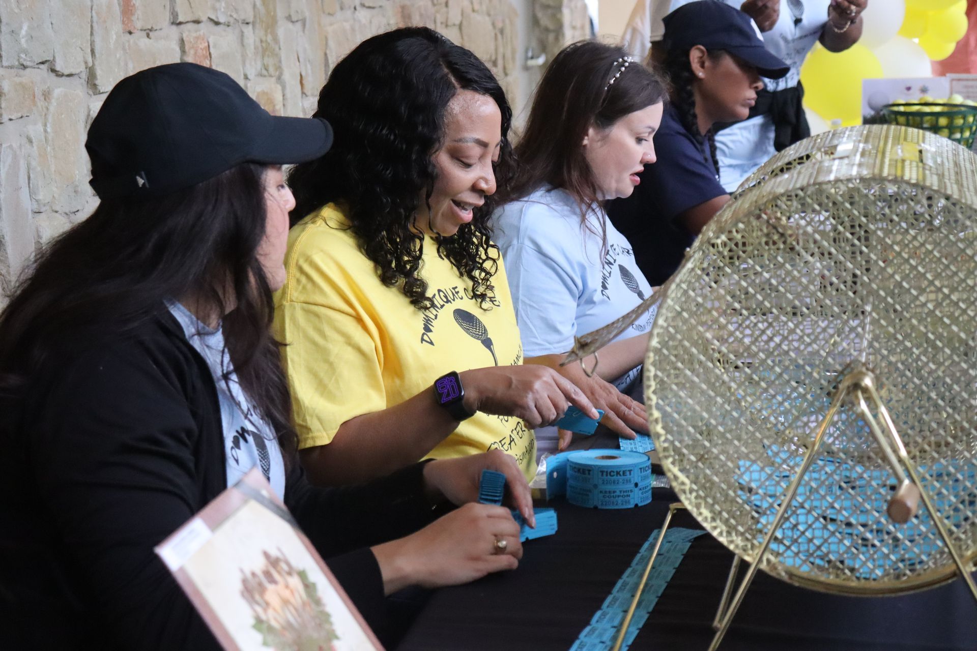 Women selecting tickets from lottery tumbler at a charity event.