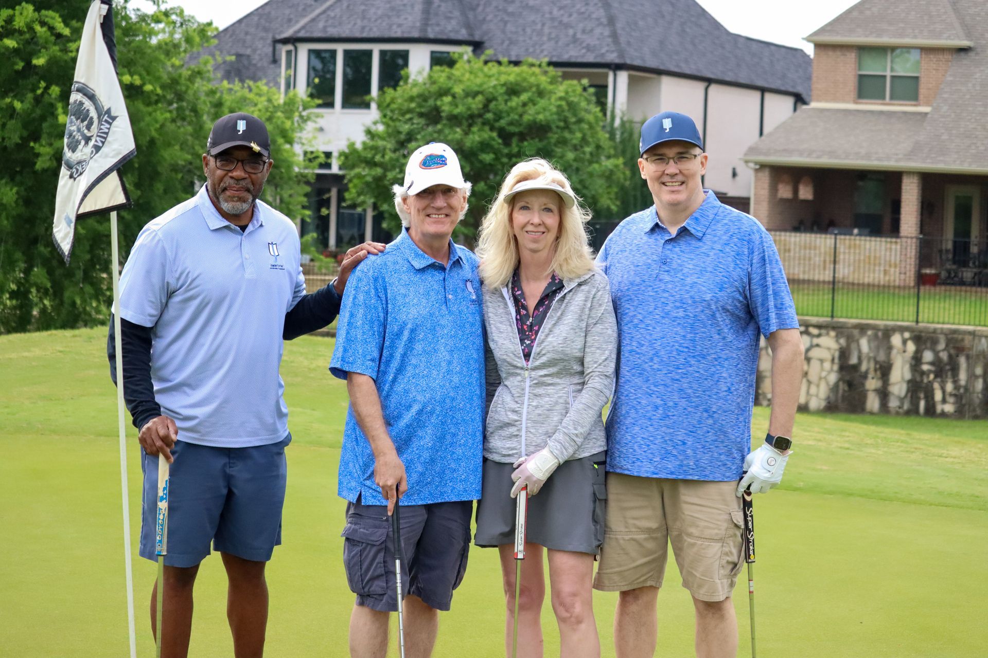 Four people pose on a golf course. Two men and a woman wear blue, another man in khaki. All are smiling.