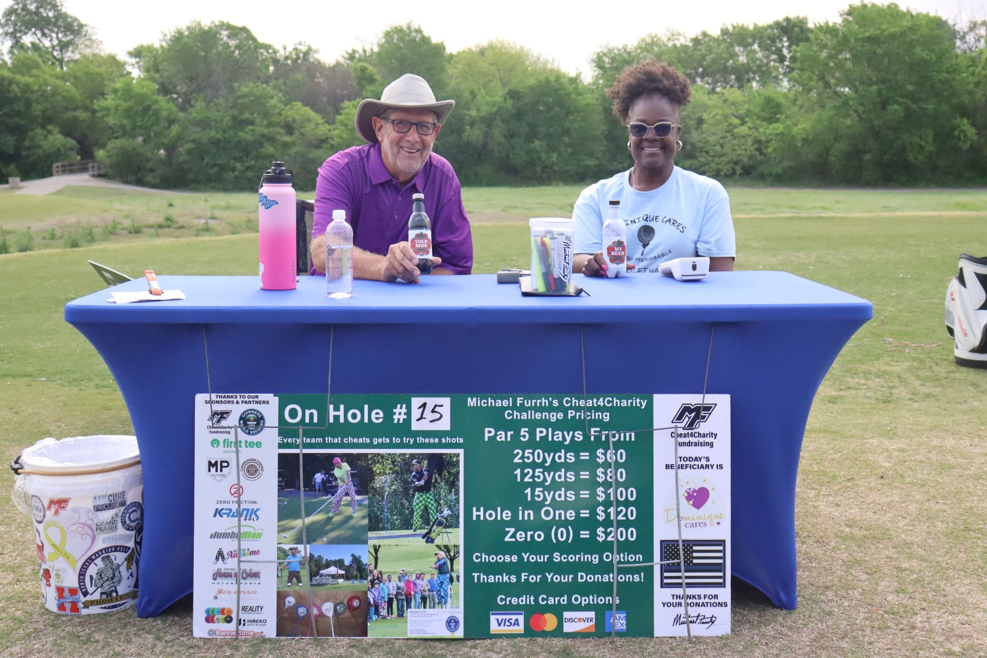 Two people at a table on a golf course. Sign for a charity golf challenge.