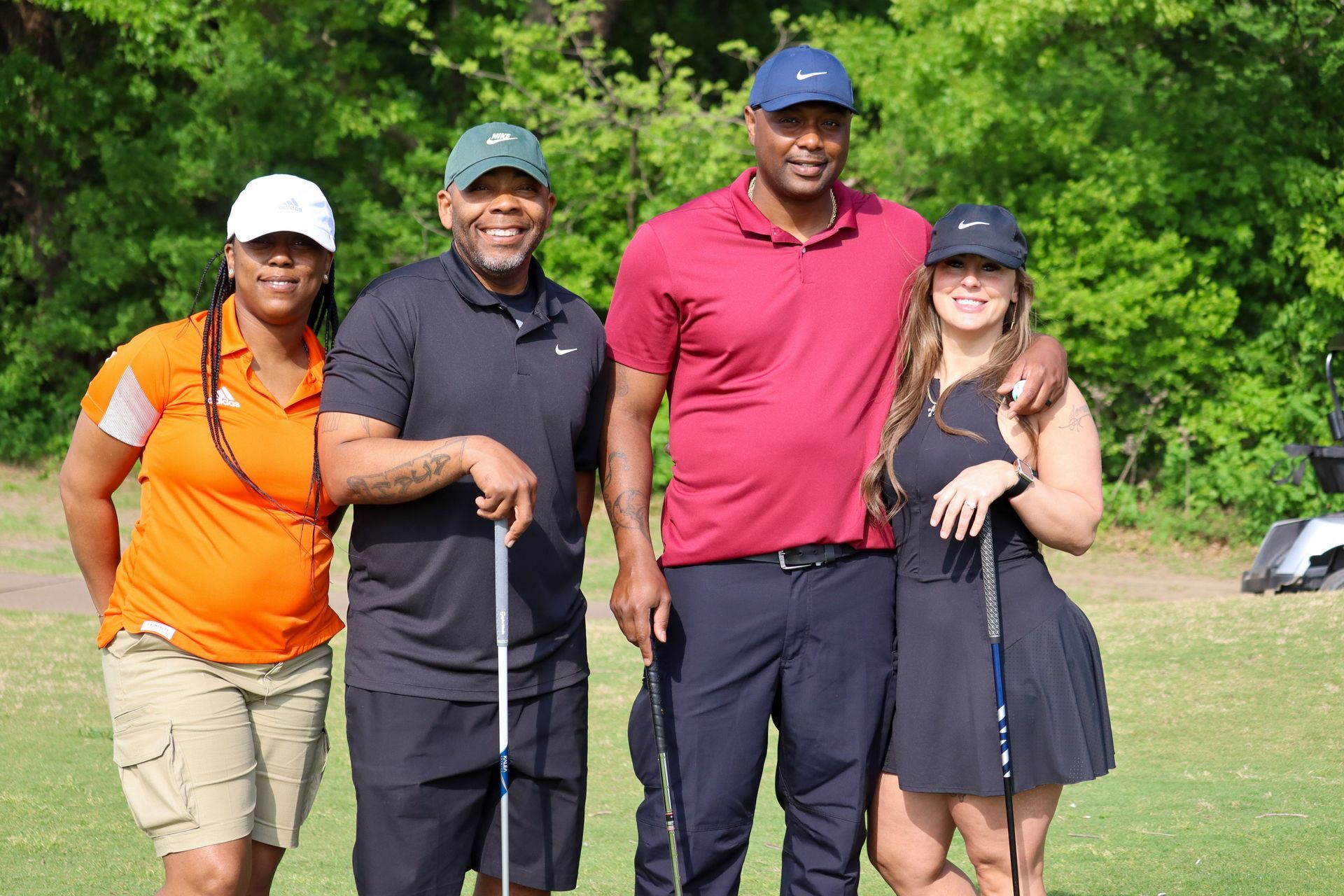 Four people smiling on a golf course, holding clubs. Two wear hats.