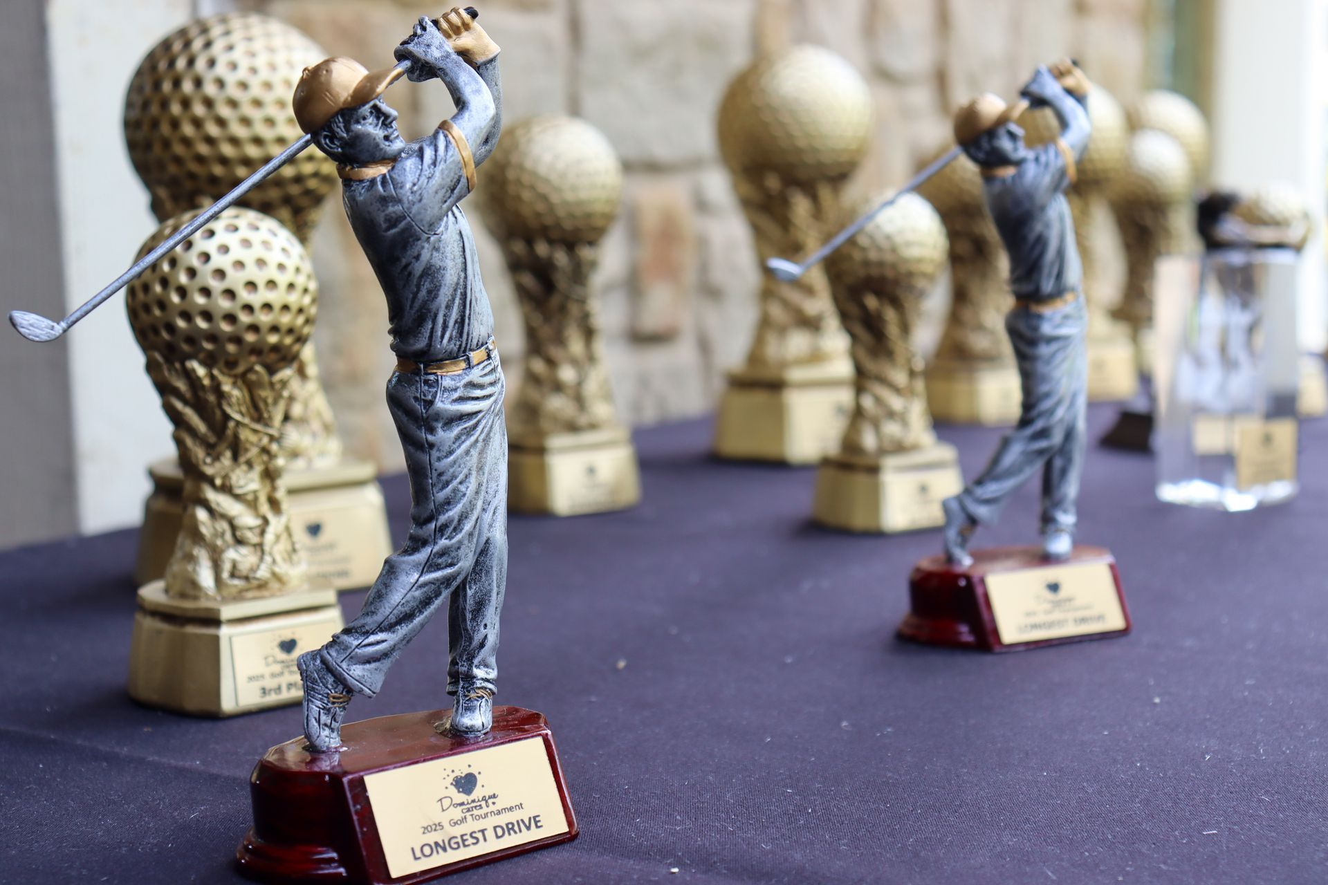 Trophies on table: golfer figurines poised to swing with golf ball shaped trophies in background.
