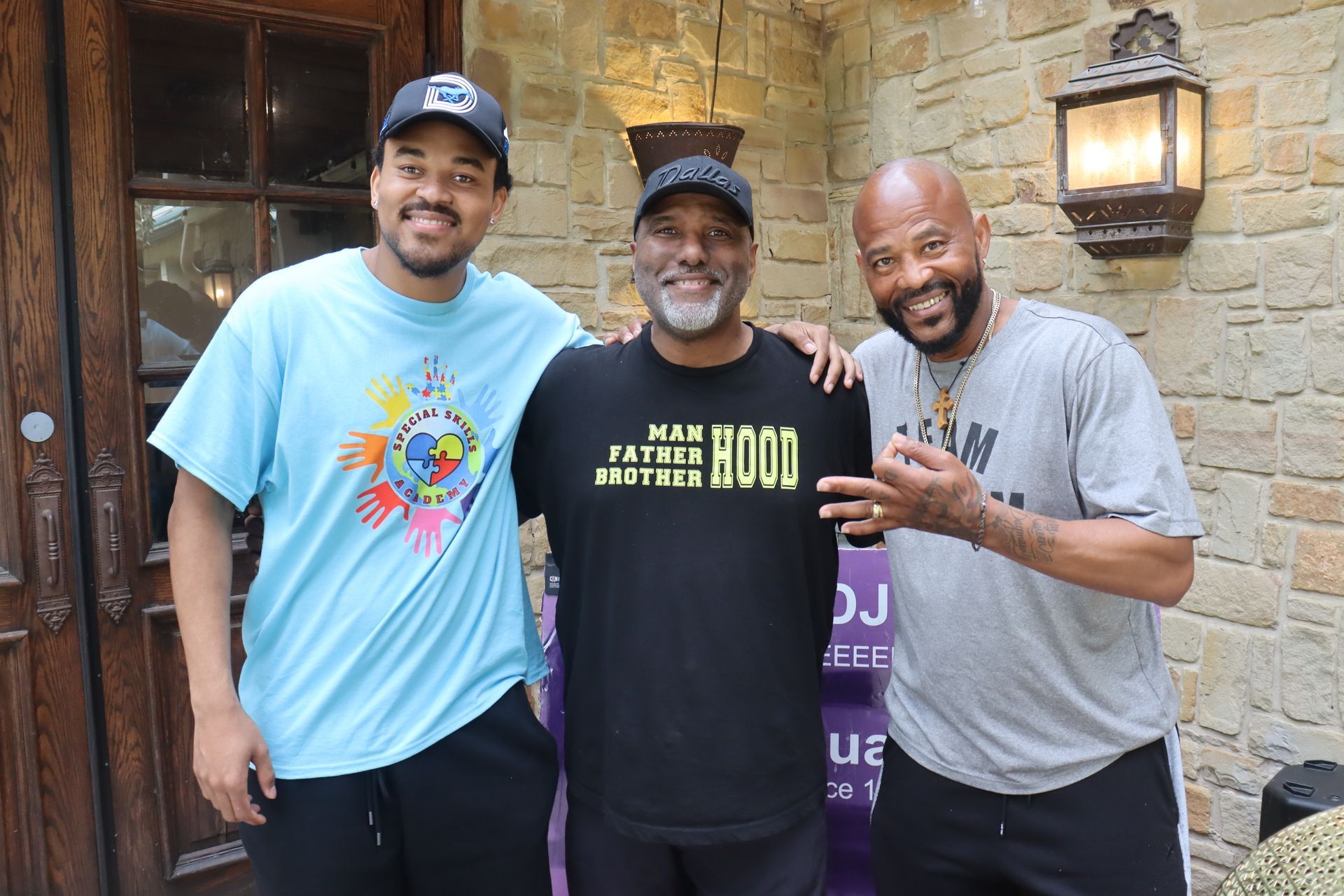 Three men standing and smiling outdoors. One wears a 