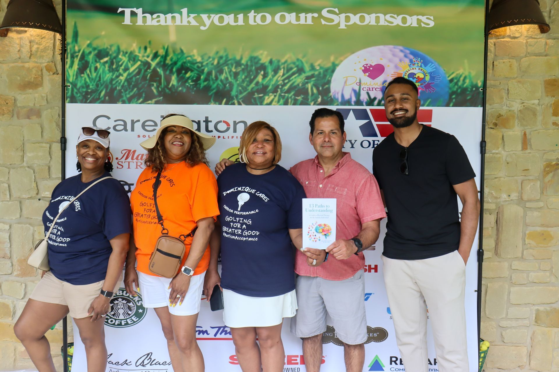 Group of five people smiling, posing near a sponsor banner at a golf event.