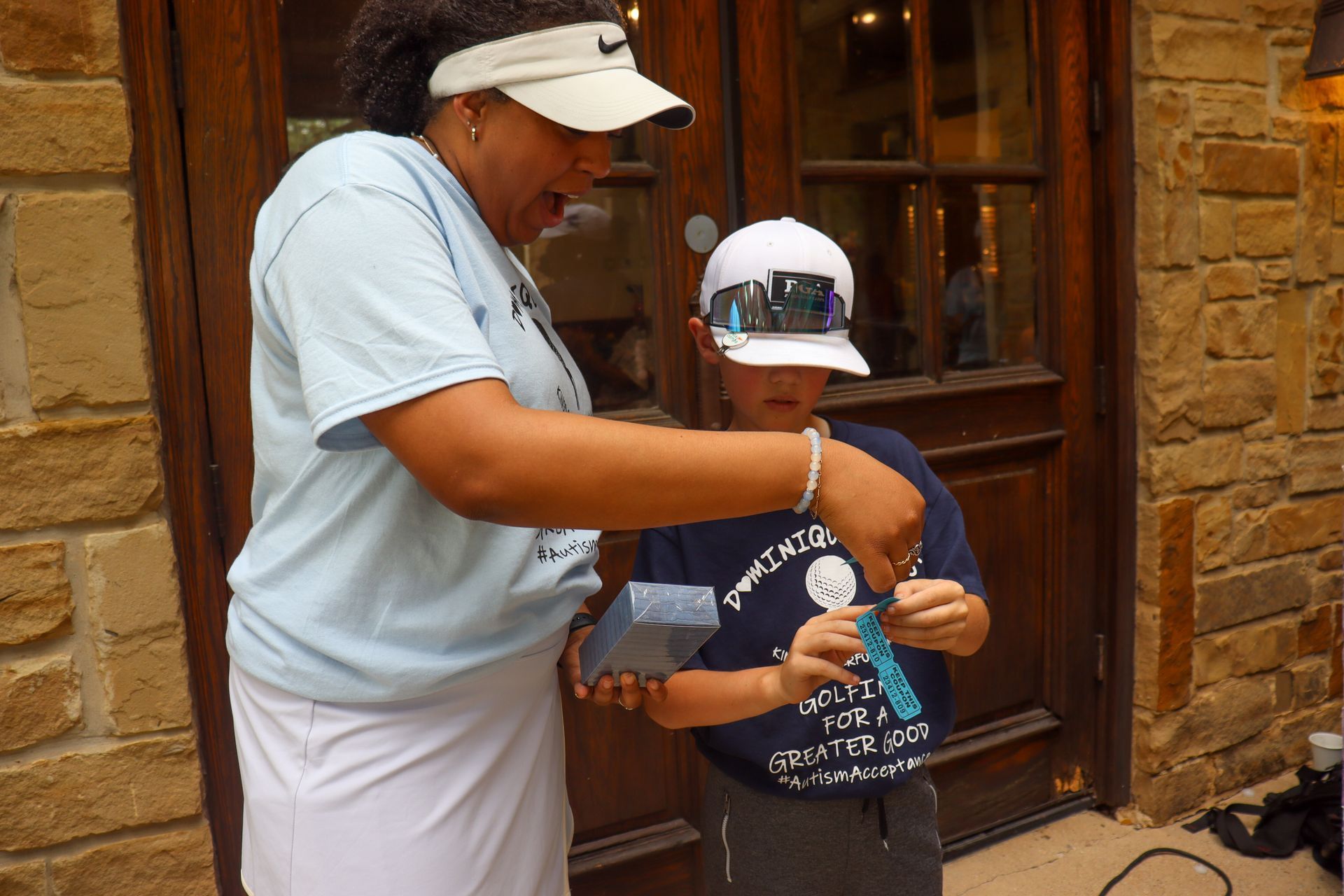 Woman showing a boy how to use something, likely outdoors. Both are wearing hats.