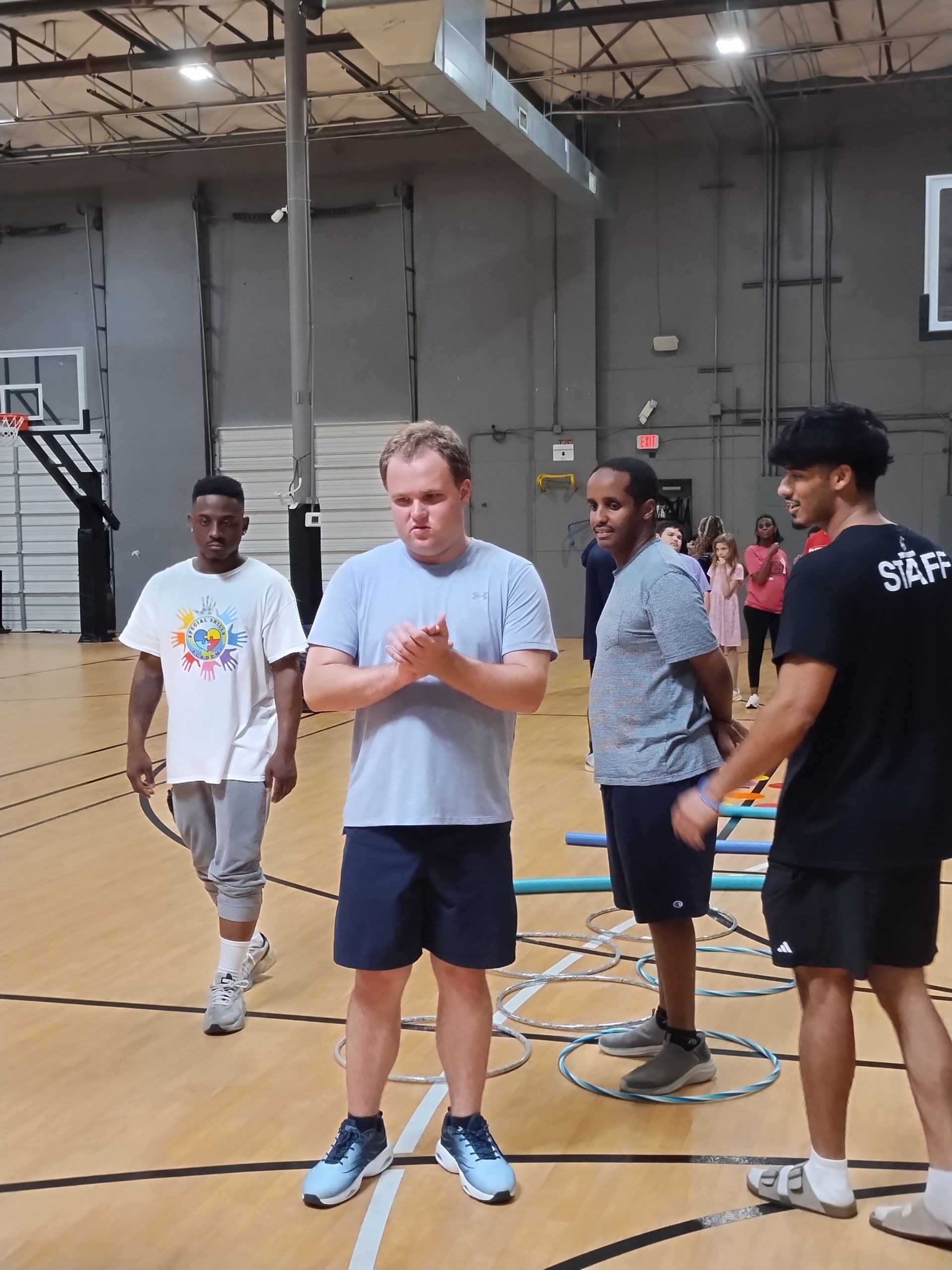 Men in a gym with basketball hoops. One claps, others watch.