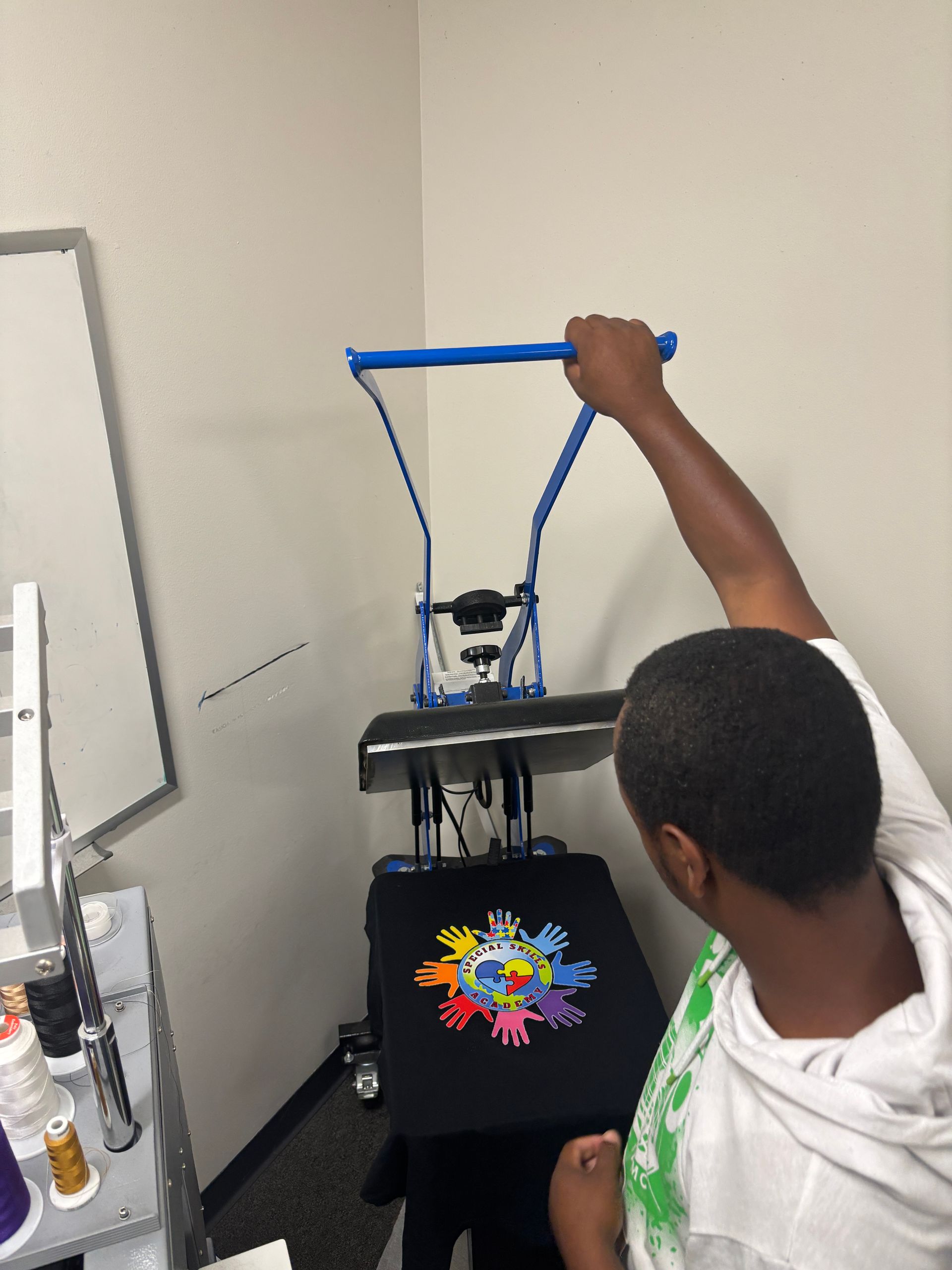 Person pressing down on a heat press, a black t-shirt with a colorful design is below. White room.