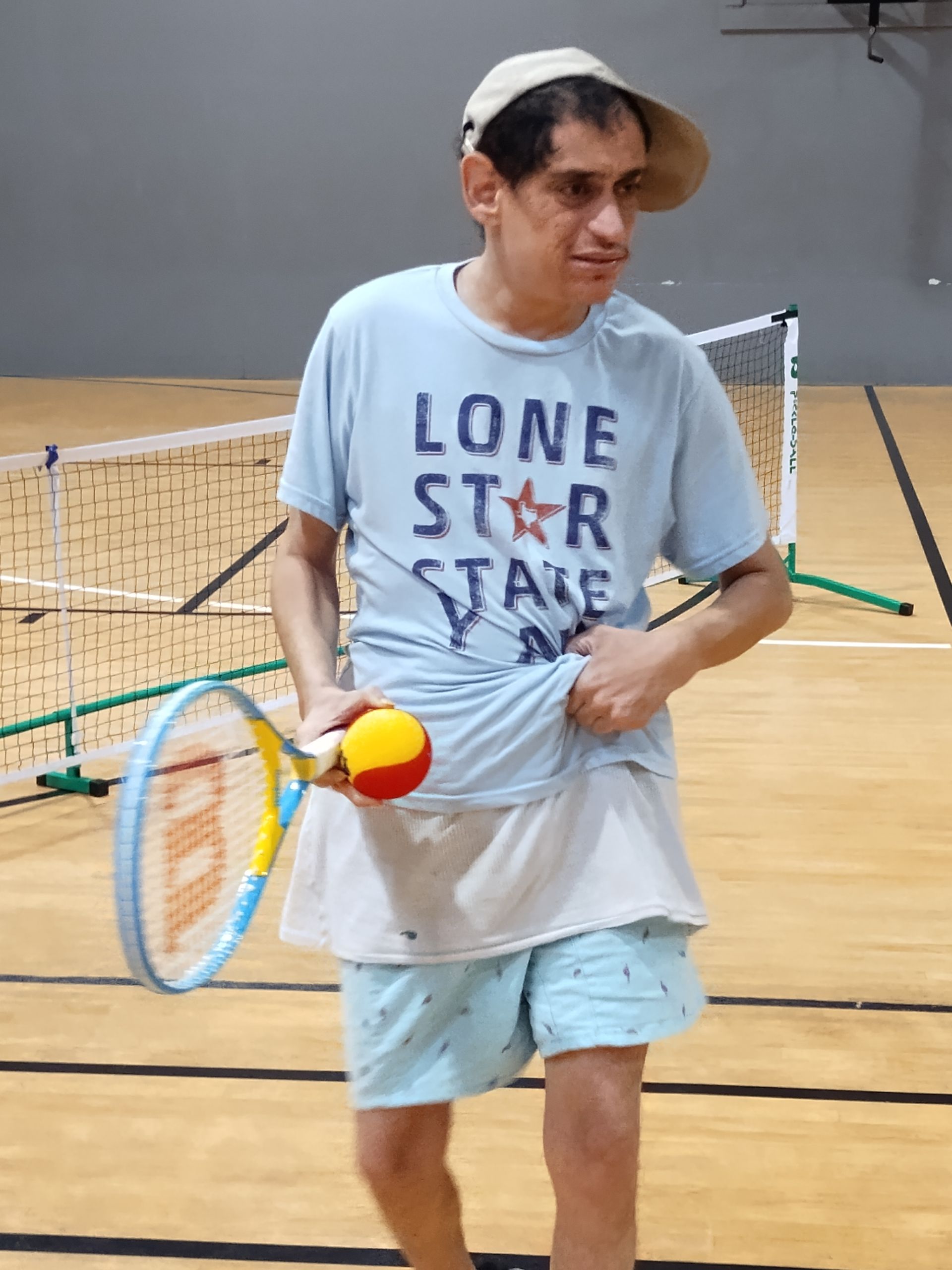 Man in Texas shirt, playing tennis indoors, holding ball and racquet.