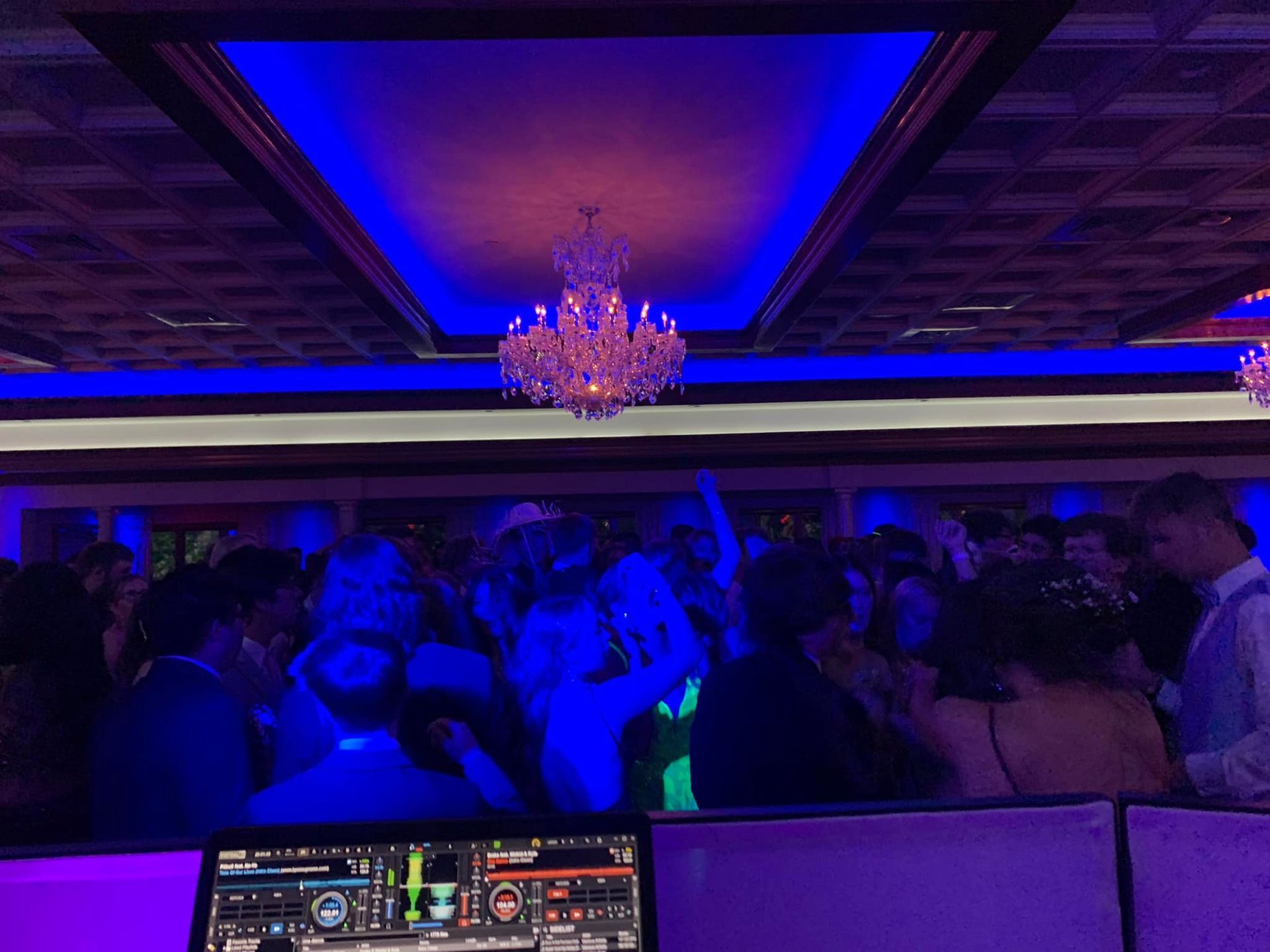 A crowd of people are dancing in a room with blue lights.