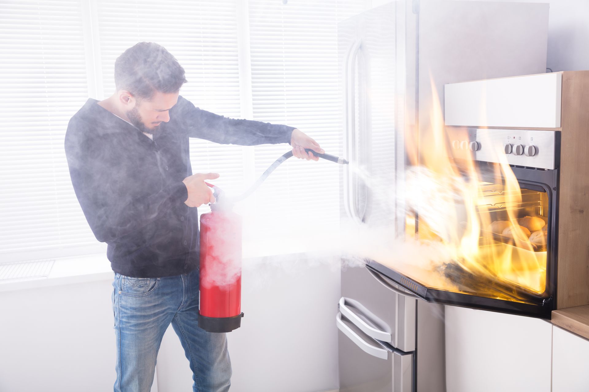 A man is using a fire extinguisher to put out a fire in an oven.
