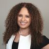 A woman with curly hair is smiling and wearing a white shirt.