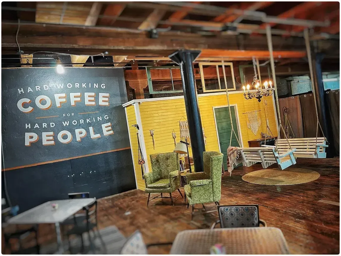 A room with tables and chairs and a sign that says `` coffee helps work my people ''.