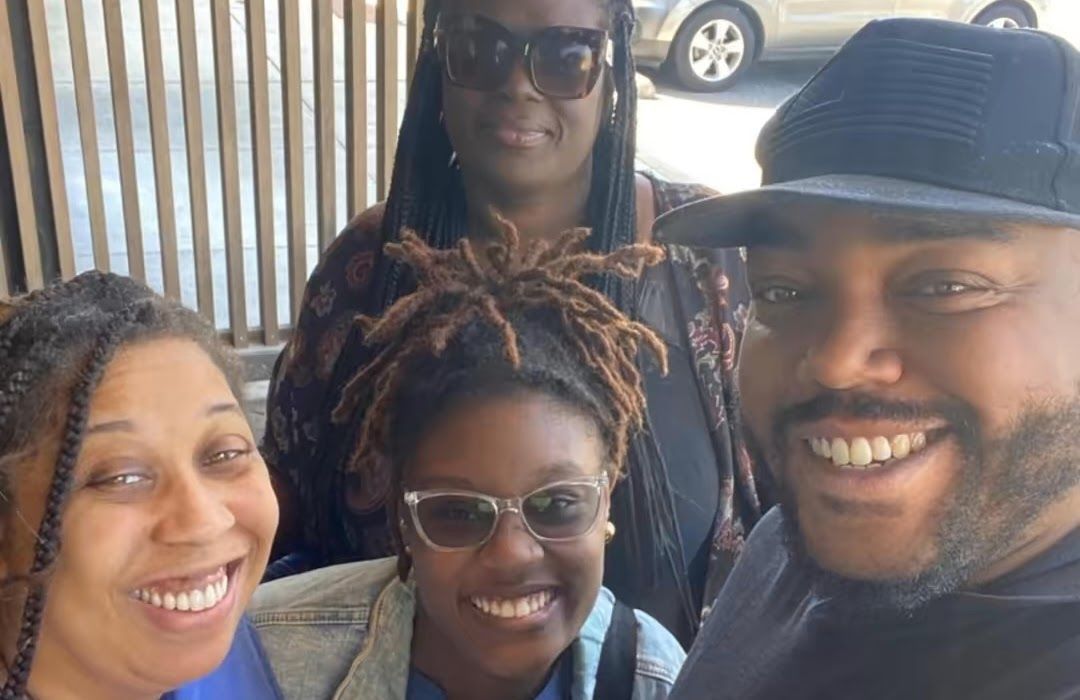 Four smiling people of color in a group selfie outdoors.