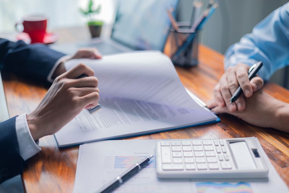 Person stamping a document during a business meeting, next to a calculator and pen.