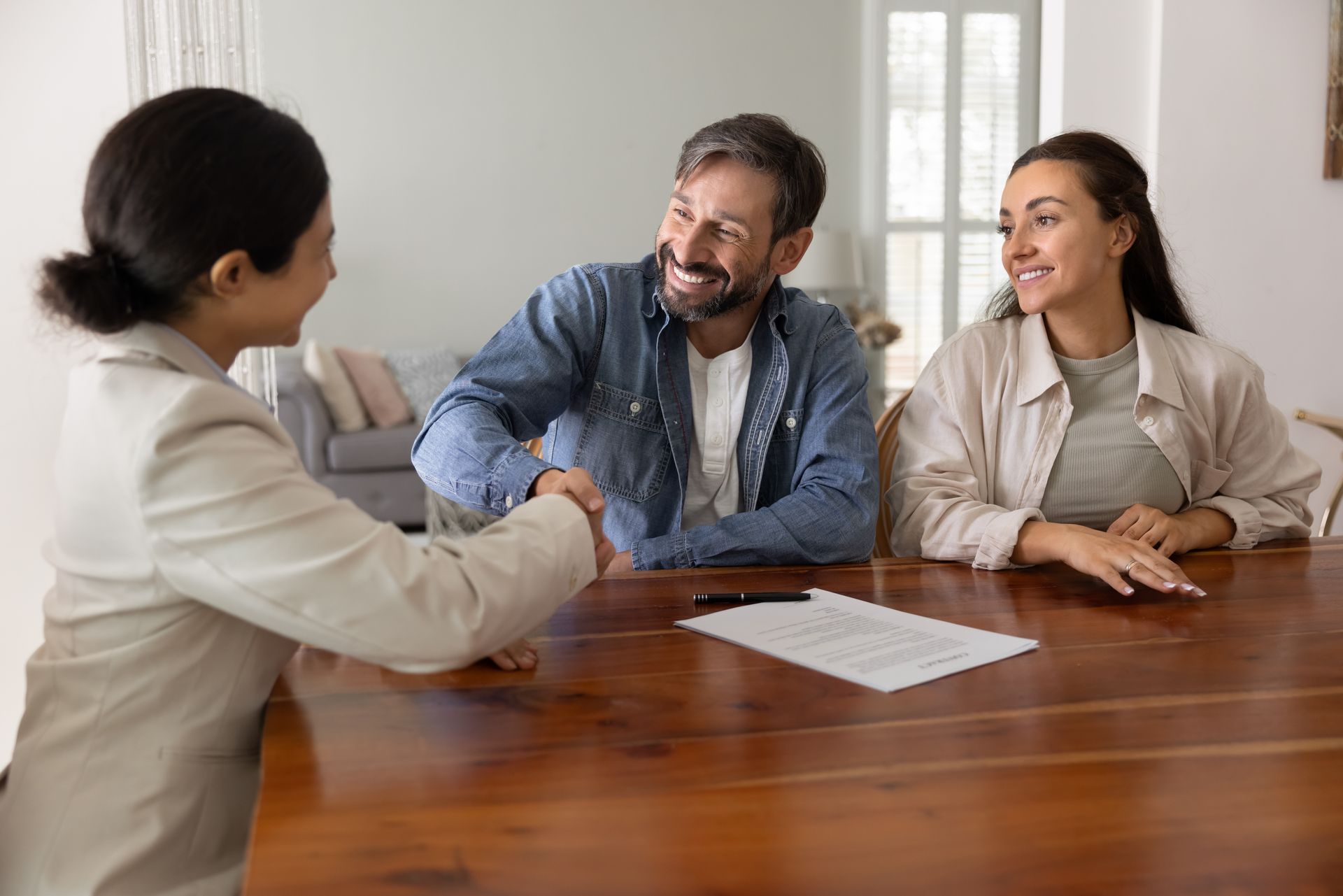 Woman shaking hands with a man across a table, with another woman present. They appear to be happy, indoors.
