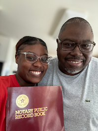 A young woman and man smiling, holding a notary public record book.