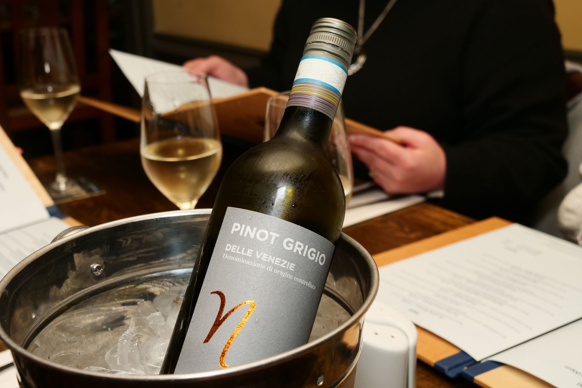 A bottle of pinot grigio wine is in a bucket of ice.