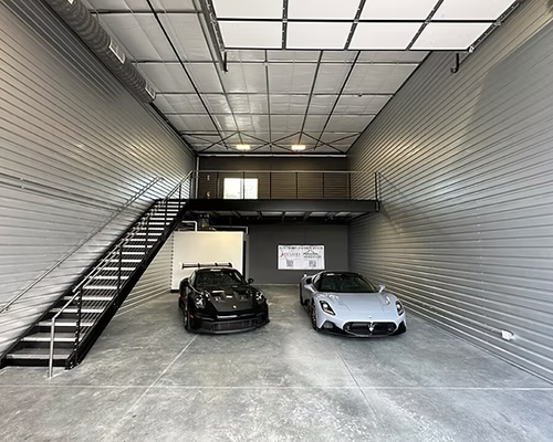 Cars parked in a modern, gray garage with a mezzanine, stairwell.