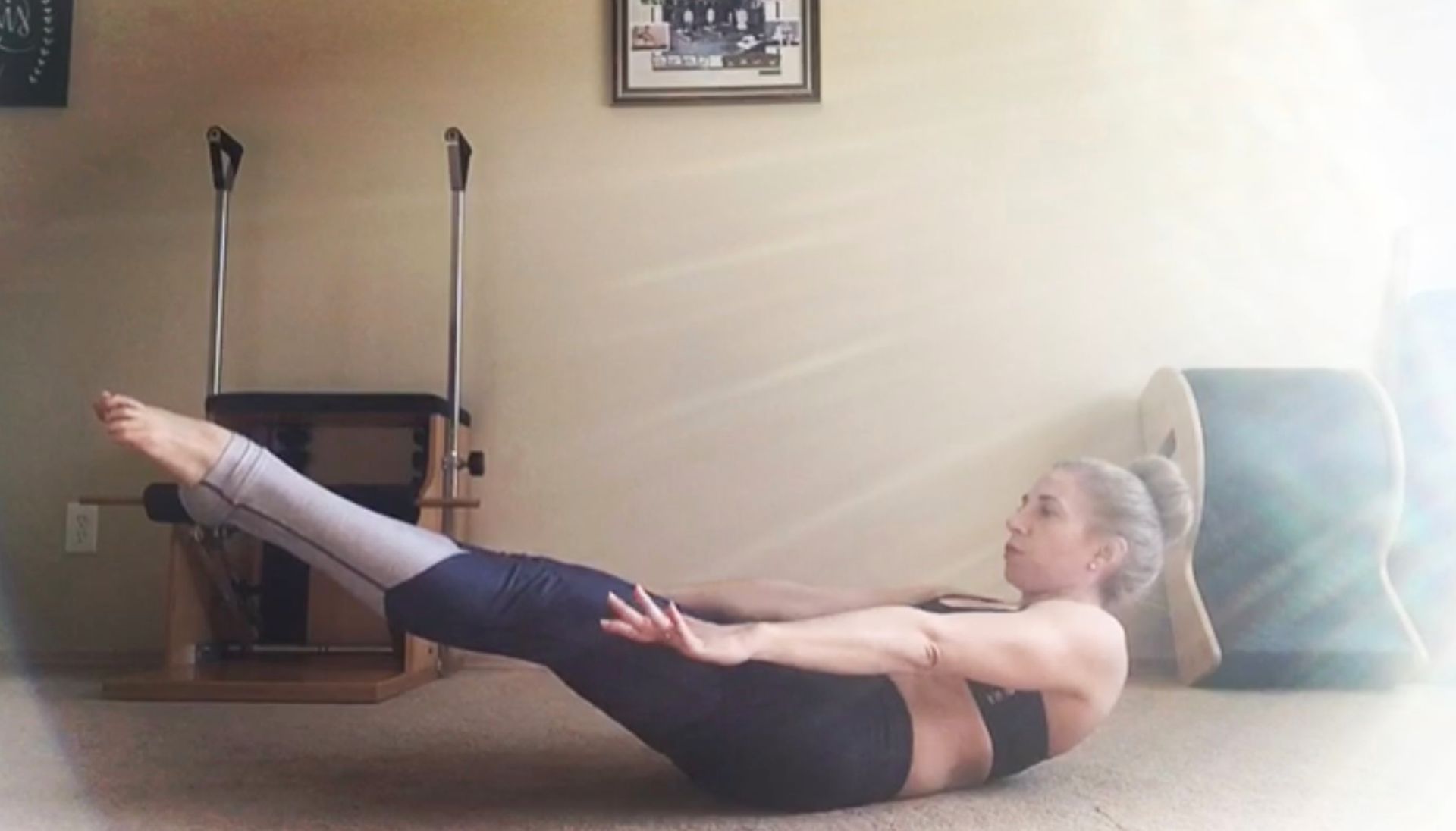 Woman doing Pilates exercise on the floor with arms outstretched, legs extended, in a room.