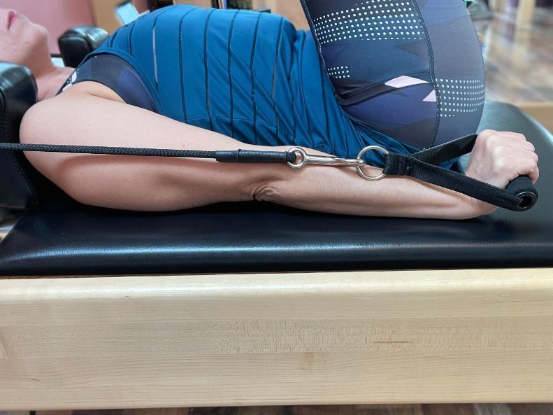 A woman is laying on a pilates machine with a resistance band.
