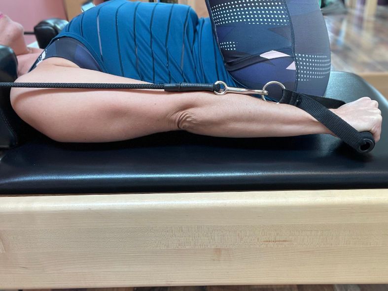 A woman is laying on a pilates machine with a resistance band around her arm.