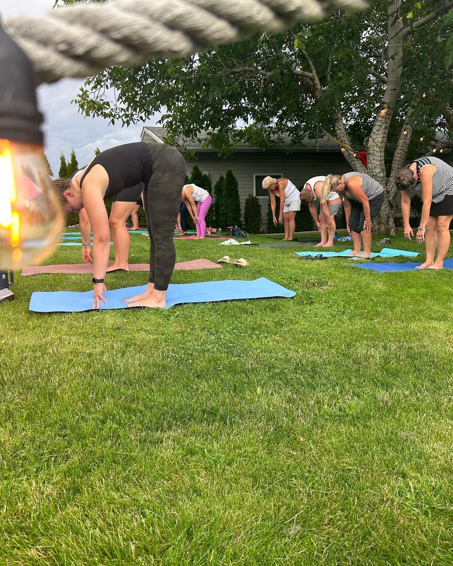 People doing yoga stretches on blue mats in a grassy yard outdoors.