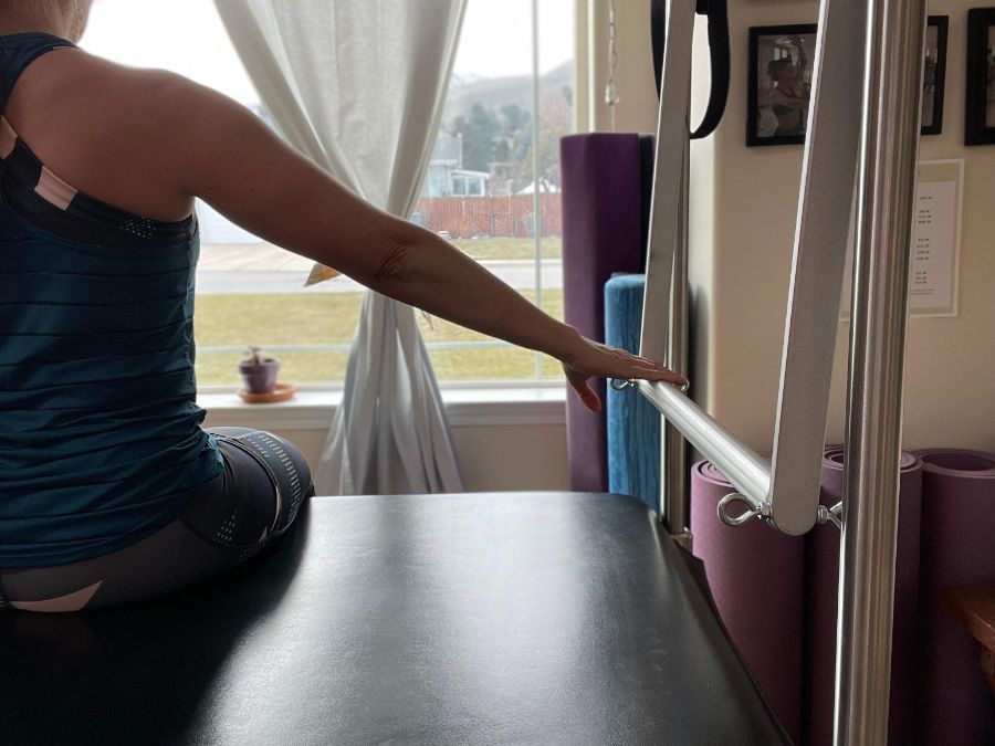 A woman is sitting on a pilates machine in front of a window