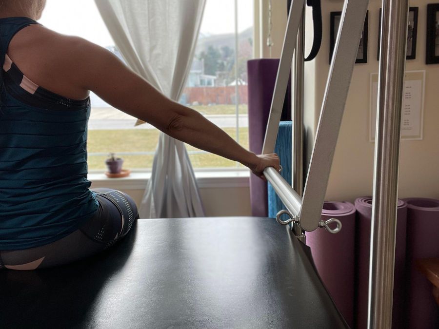 A woman is sitting on a pilates machine in front of a window