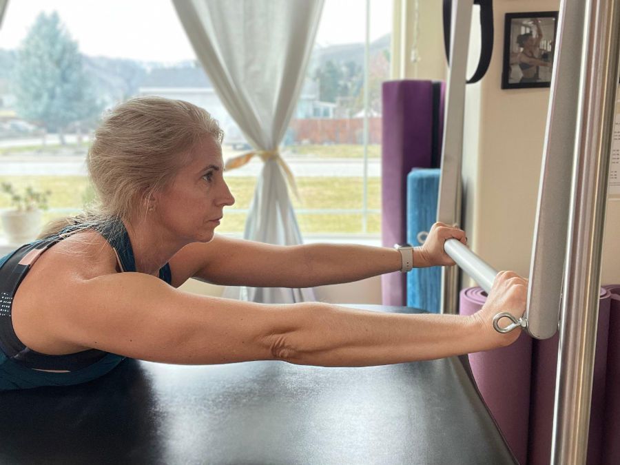A woman is stretching her arms on a pilates machine.
