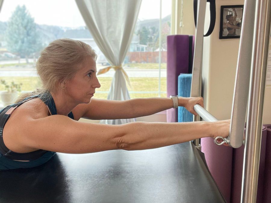 A woman is stretching her arms on a pilates machine.