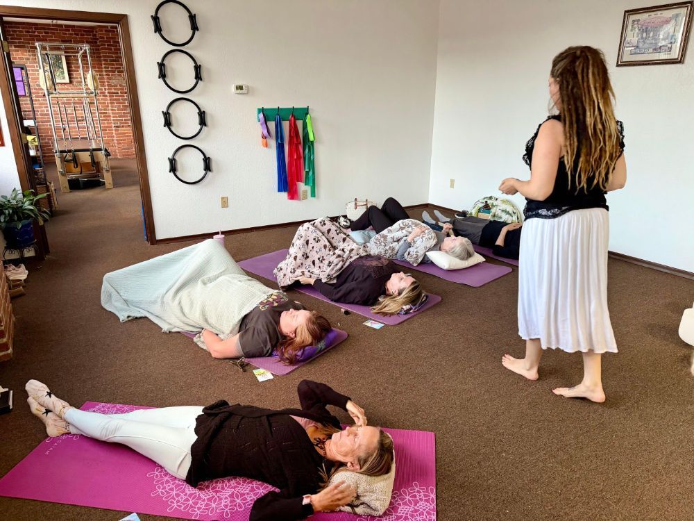 Children resting on mats in a room while an adult stands nearby.