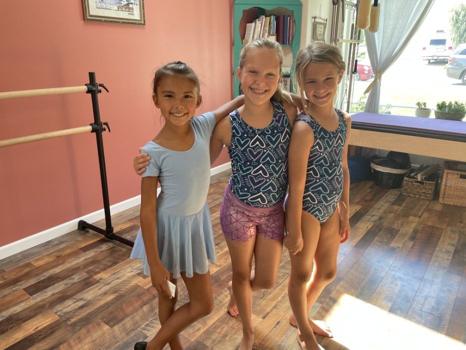 three young girls are posing for a picture in a dance studio .