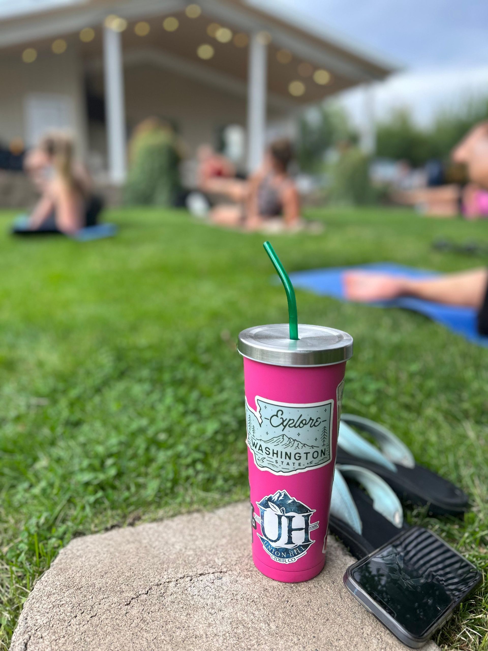 a pink cup with a green straw is sitting on a rock in the grass
