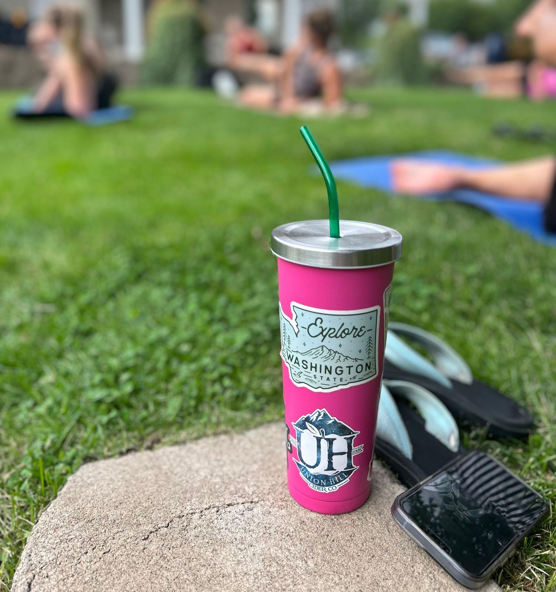 A pink cup with a green straw is sitting on a rock.