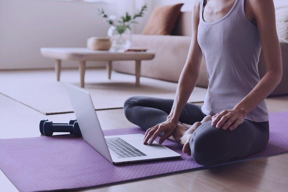 a woman is sitting on a yoga mat using a laptop computer .