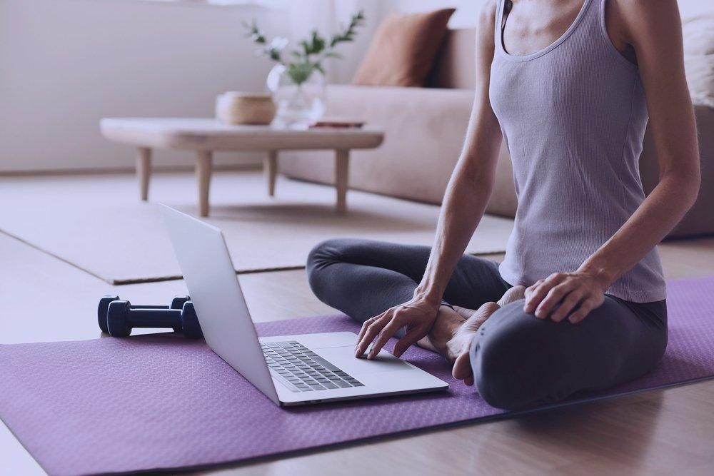 A woman is sitting on a yoga mat using a laptop computer.