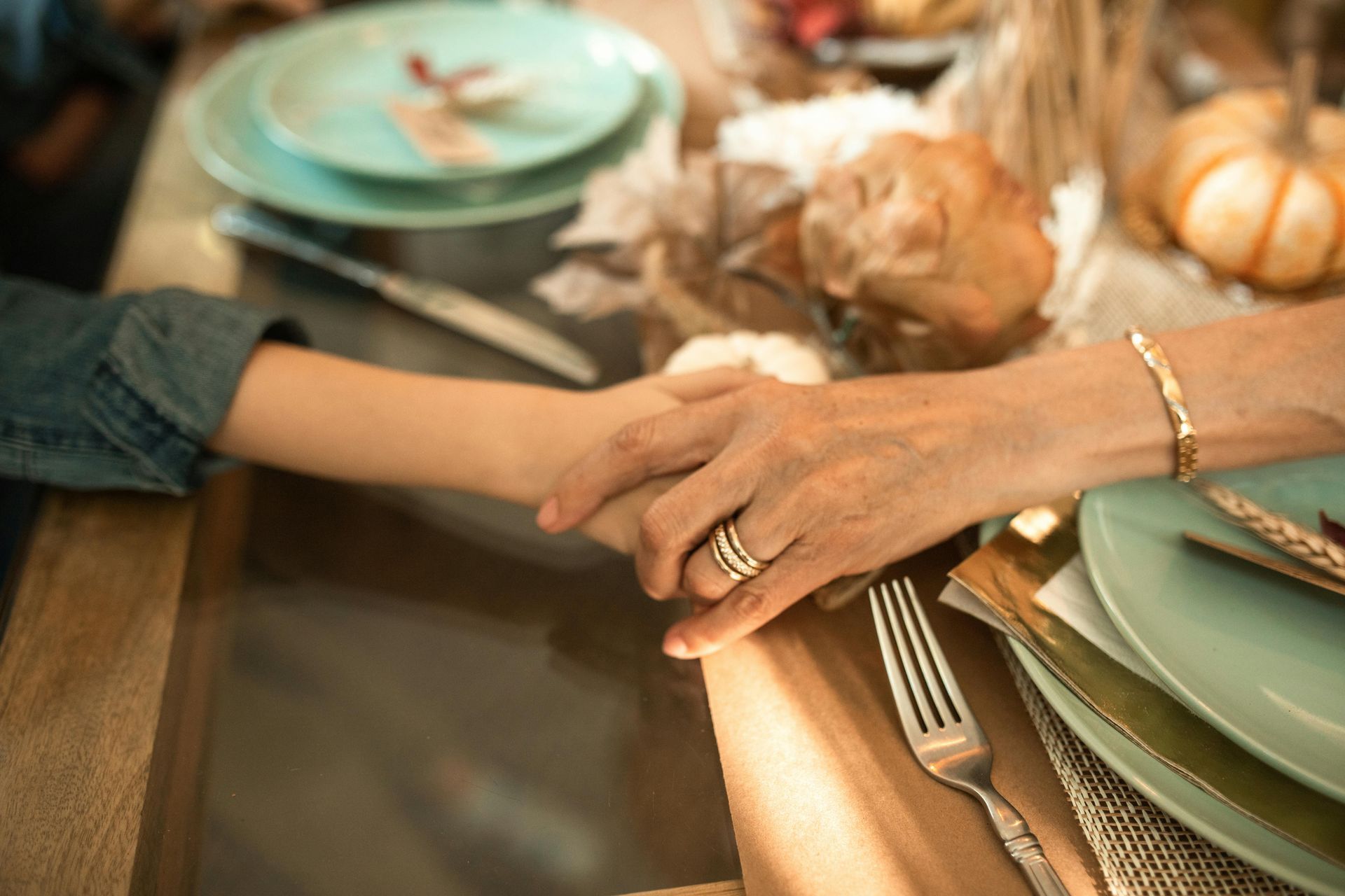 Hands clasped at a Thanksgiving table, near a plate and decorations.